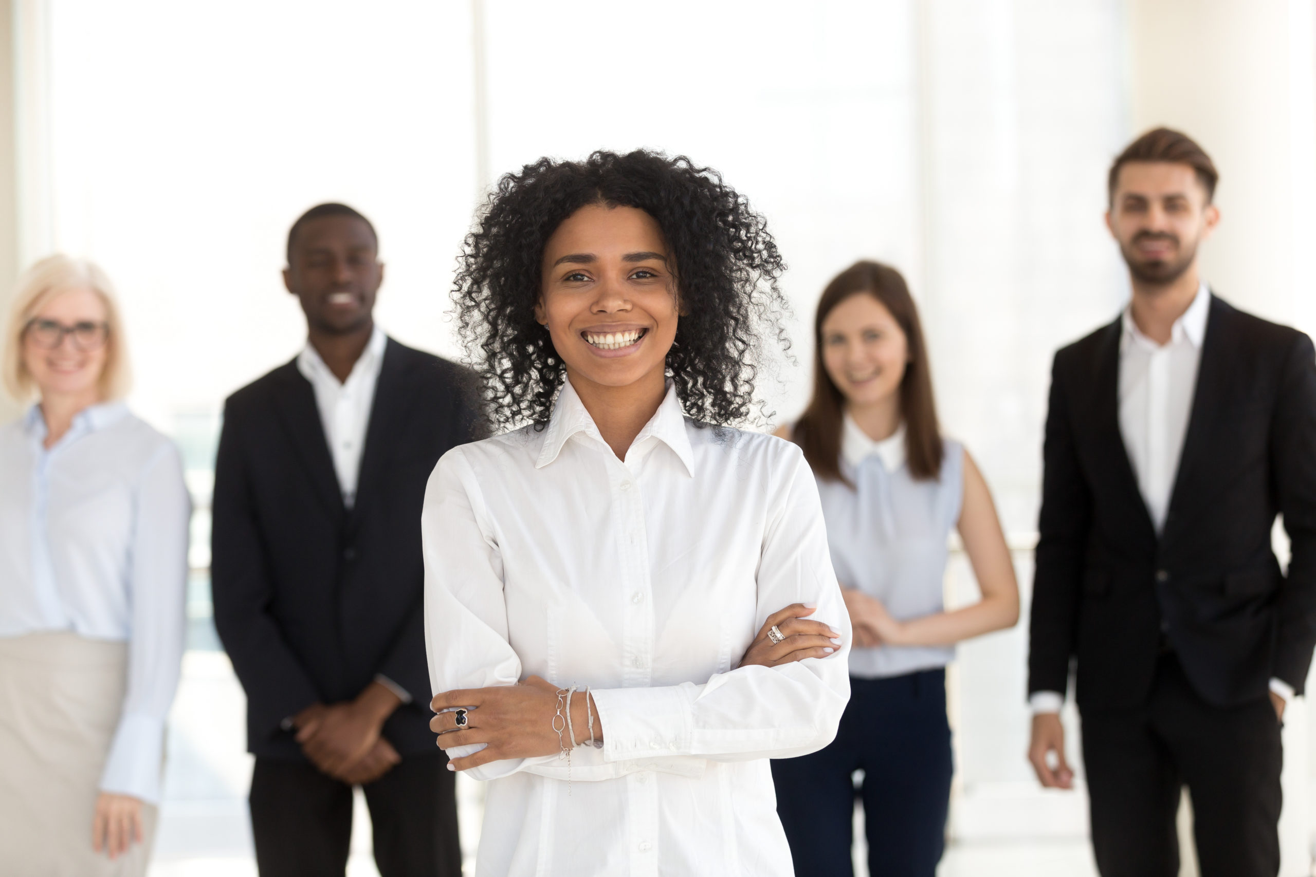 Smiling young african corporate employee executive, mixed race office worker, female black business coach, millennial professional looking at camera standing with diverse team in office, portrait