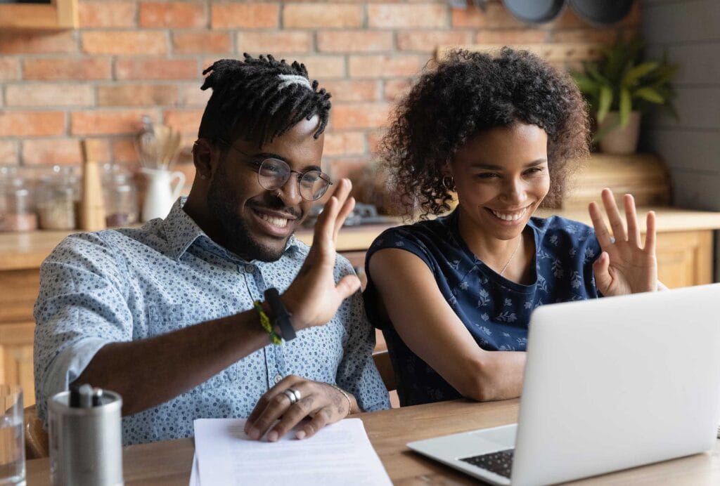 A male and a female in front of a laptop waving their hands