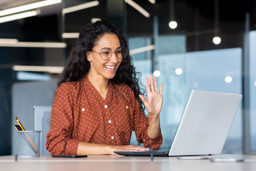 A woman smiling and waving in front of the laptop