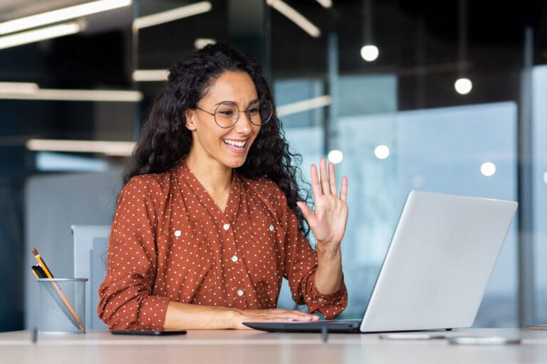 A woman smiling and waving in front of the laptop