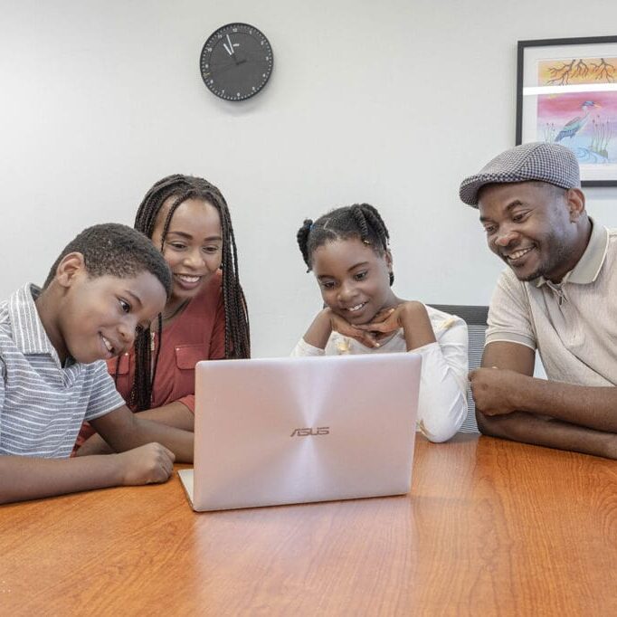 A family of four around a table smiling and looking at a laptop