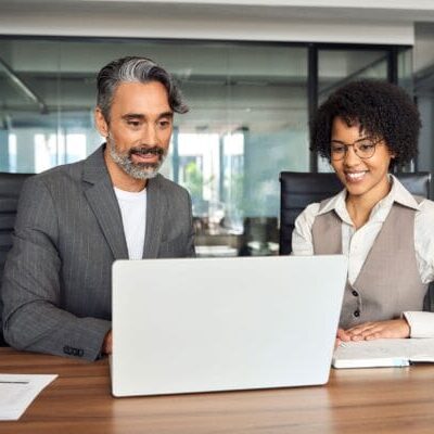 A male and female sitting next to each other in front of laptop