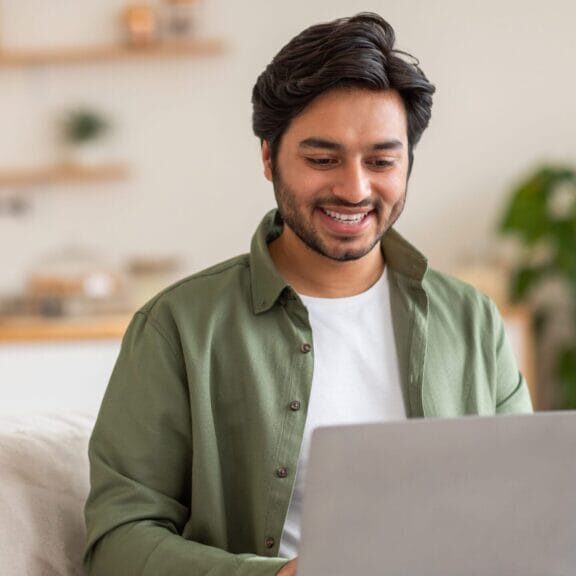 Man sitting on the couch smiling and using his laptop